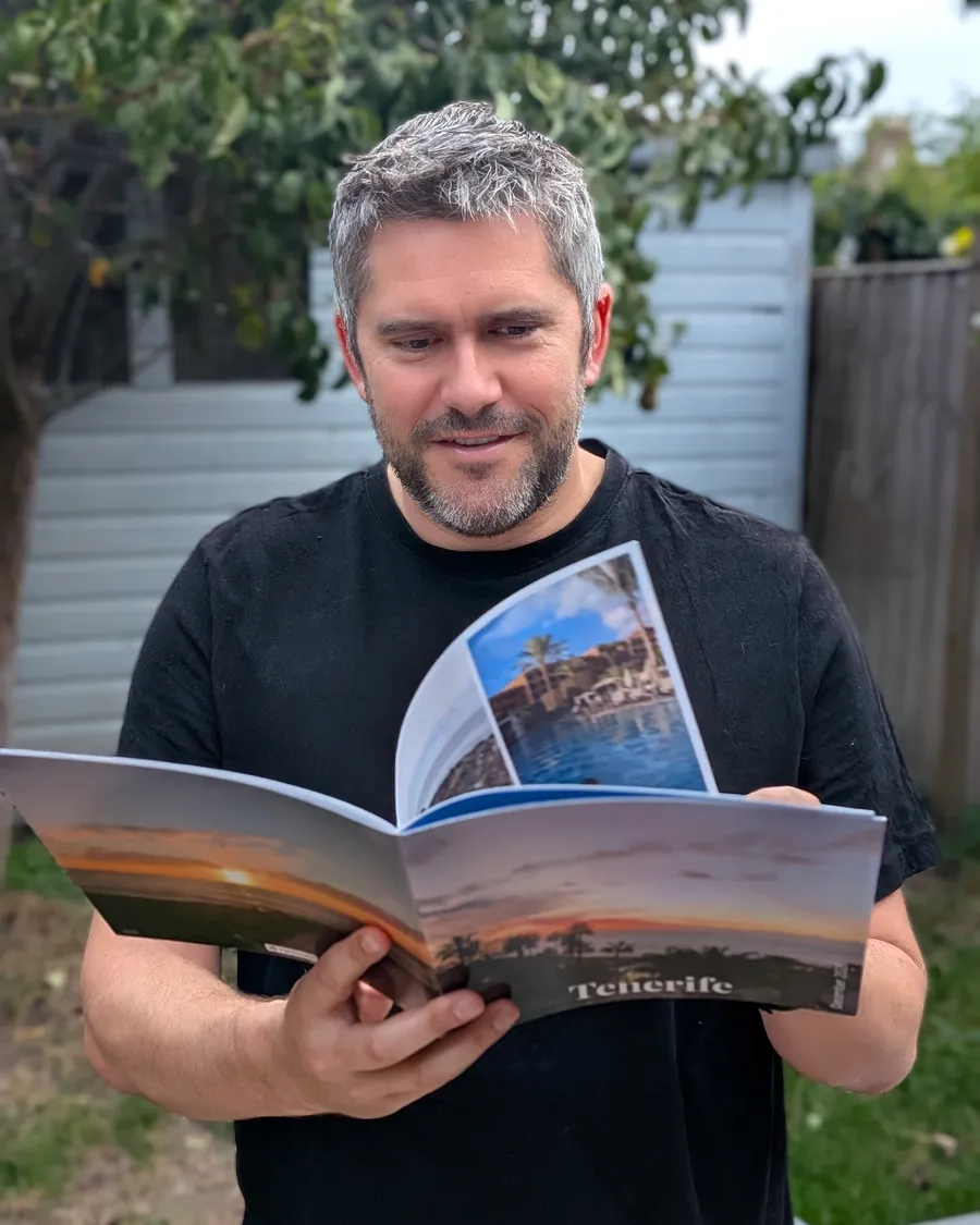 Jake Gordon smiling as he turns the pages of an RGBloom photo book titled Tenerife