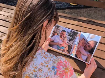 Someone on a garden bench turning a page of a printed book, photographs on every page