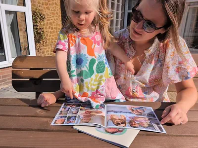 A small child pointing at a photograph in an open printed book while a woman leans in to look