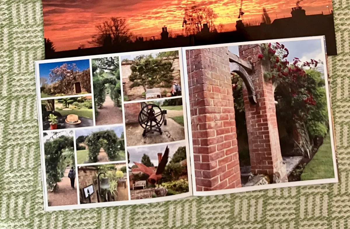 An open photo book of garden photos, a brick arch hung with red roses on one page and a grid of smaller photos on the other, a sunset print behind it